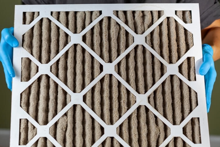 gloved hands holding a clogged air filter